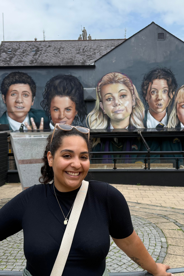 Halimah Smith Halimah standing outside in front of a mural of five people