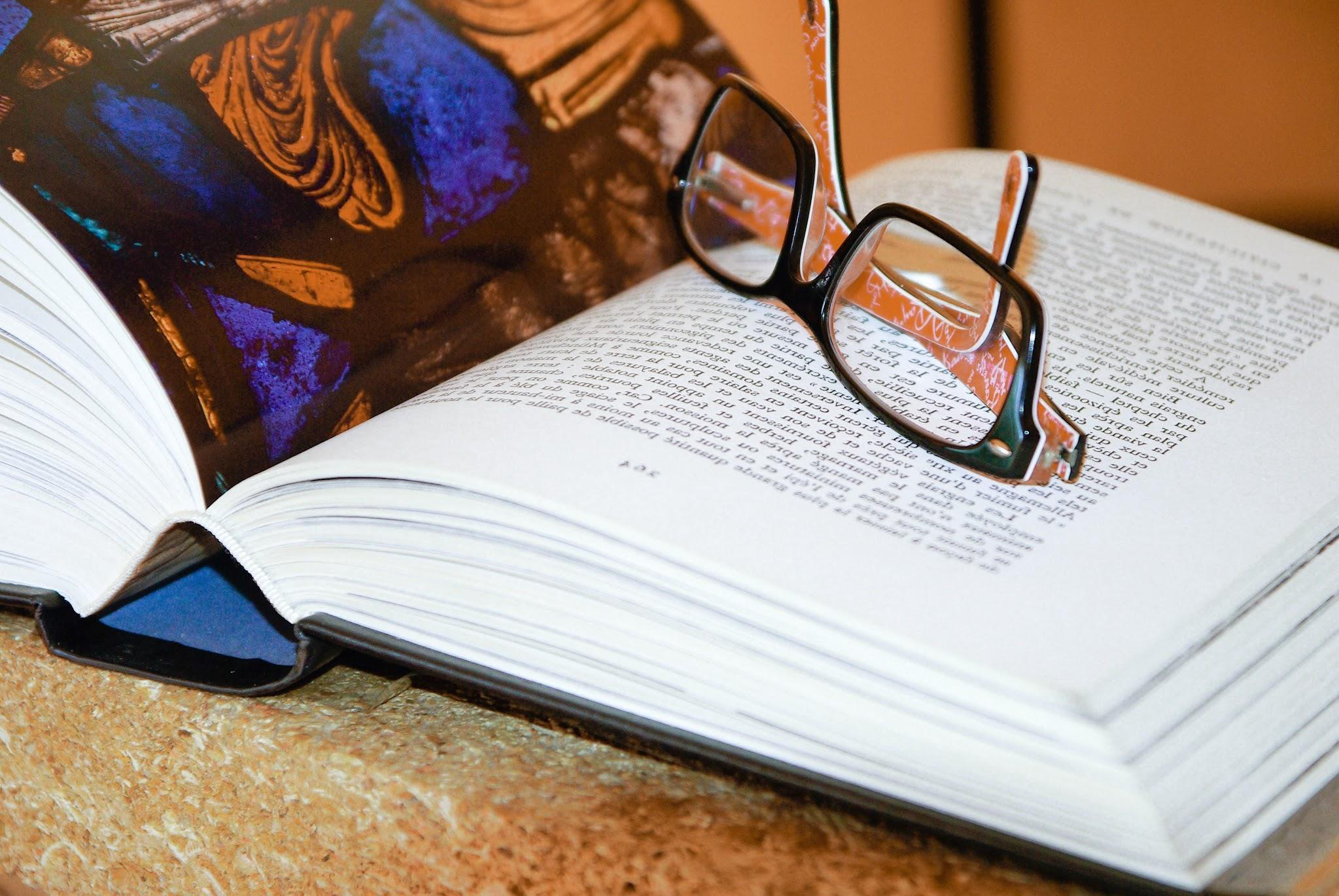 Open book and reading glasses on a desk.