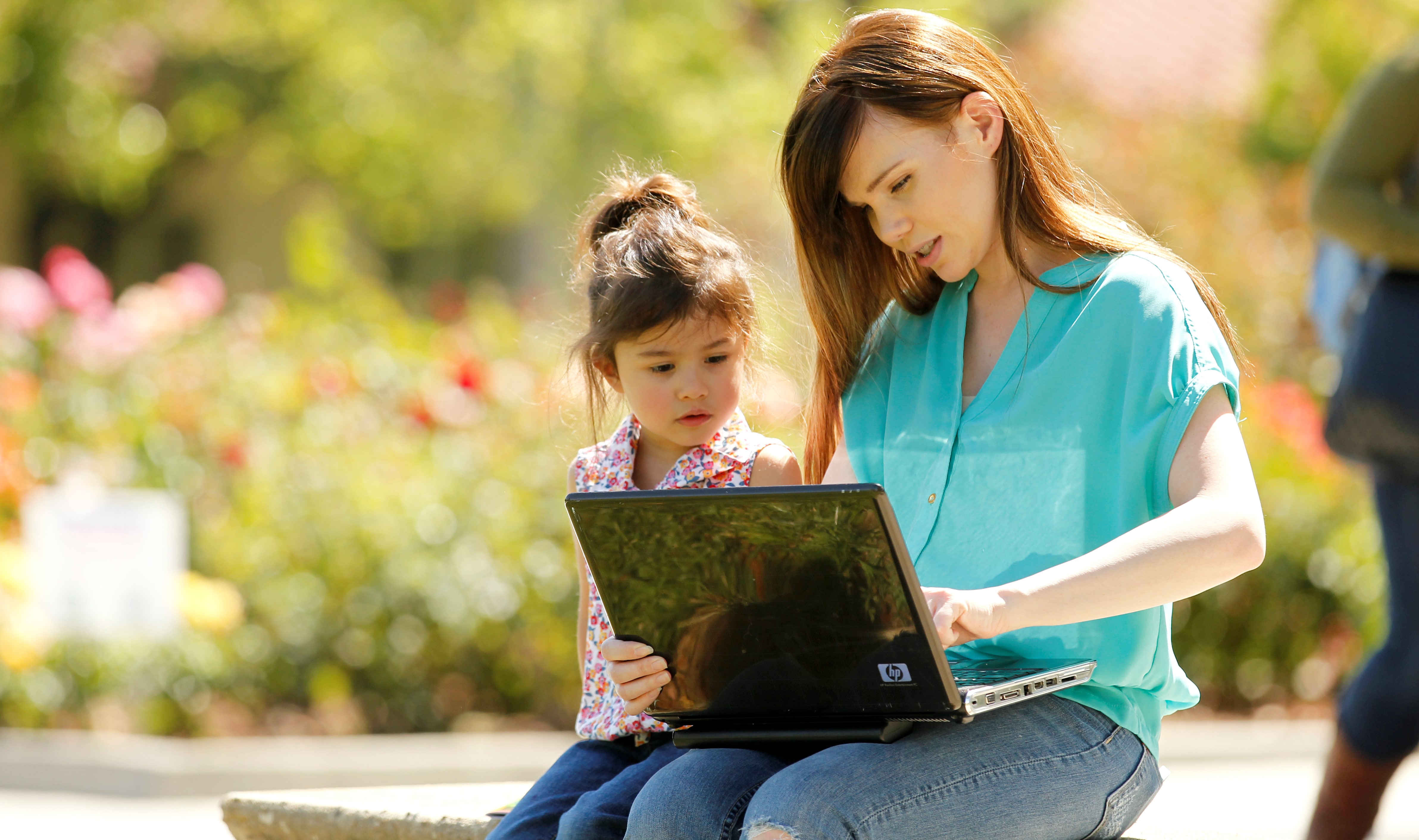 woman and a child sitting outside with a laptop 