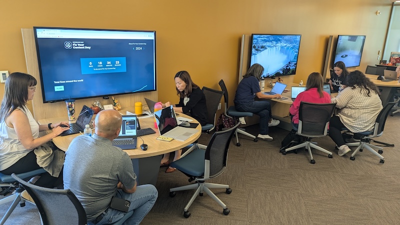 8 faculty members around tables in the IDEAS lounge working on their laptops