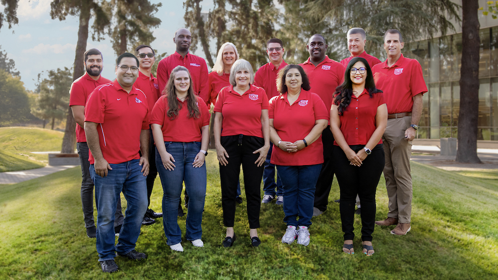 All members of the Office of IDEAS team pose together in the Fresno State Peace Garden just outside the university library, each wearing a red Fresno State shirts