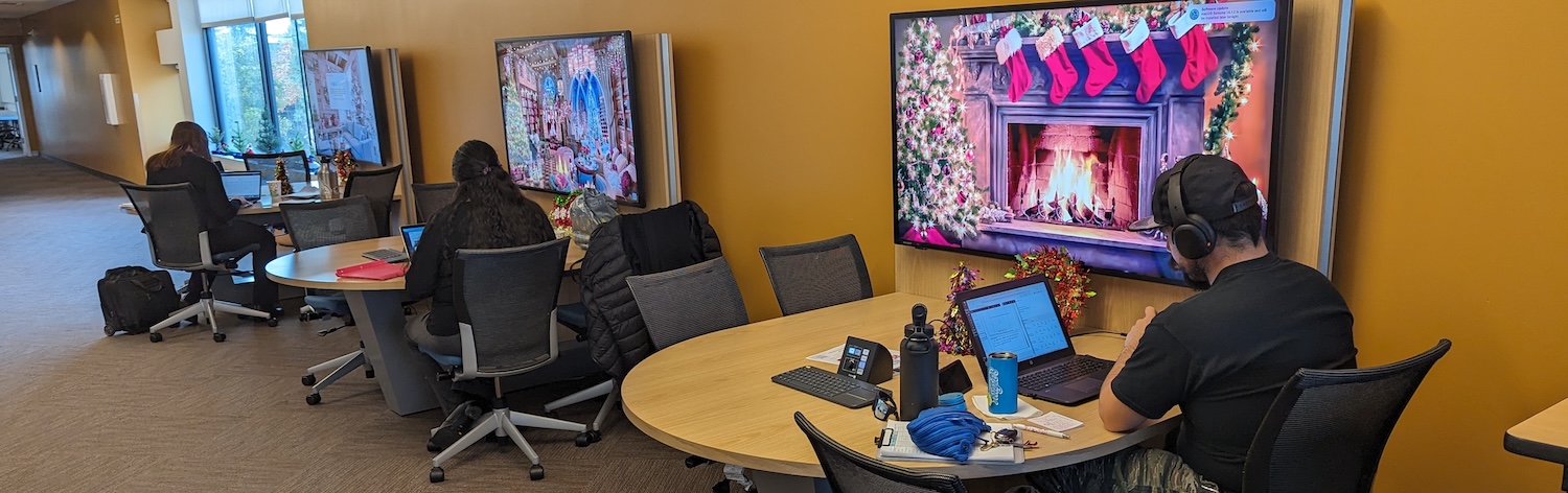 Faculty working in the IDEAS lounge with holiday imagery on the large screens